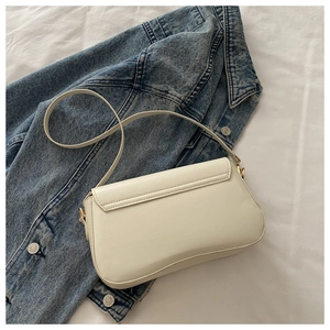 Détail du sac baguette blanc cassé avec boucles dorées sur une veste en jean
