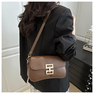 Detail of a brown leather crossbody bag with a gold geometric clasp on a black blazer