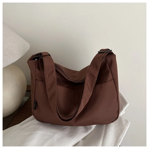 Detail of dark brown nylon tote bag with wide strap on a textured tabletop