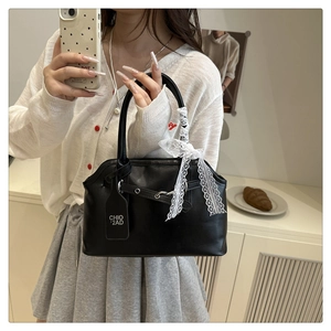 Close-up of black shell bag featuring white lace ribbon and branding tag details