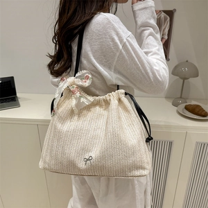 Chic beige straw tote bag with pink lace bow and drawstring, shown on model's shoulder