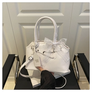Detail of white shell handbag featuring lace bow and branded logo tag on a seat