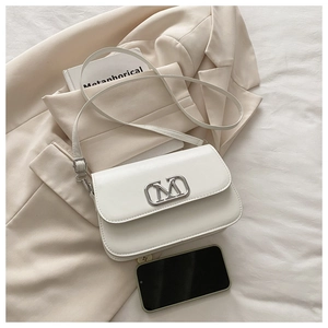 Détail du mini sac bandoulière en cuir blanc avec boucle M argentée à côté d'un smartphone
