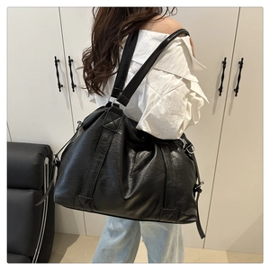 Detail of a black leather tote bag with wide straps and metal rings worn by a model