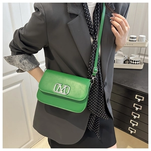 Détail du petit sac vert en cuir avec fermoir métallique M sur un tailleur gris