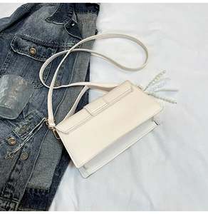 Detail view of a white rectangular crossbody bag with golden hooks on denim jacket