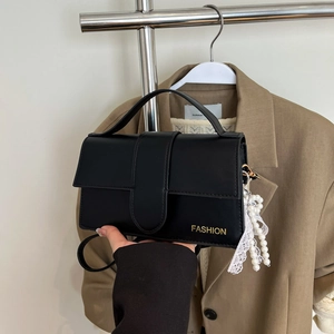 Detail of black leather handbag with gold Fashion text and pearl lace pendant charm
