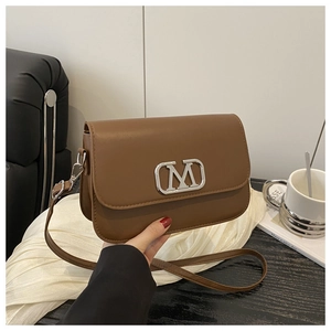 Vue détaillée du sac bandoulière marron avec logo M argenté sur un bureau élégant
