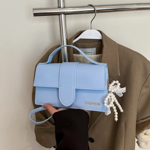 Detail of light blue crossbody bag with gold FASHION text and pearl lace charm