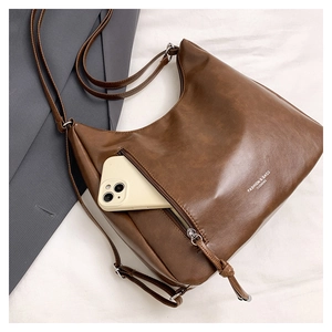 Detail of a brown leather tote bag showing a side zipper pocket holding a smartphone