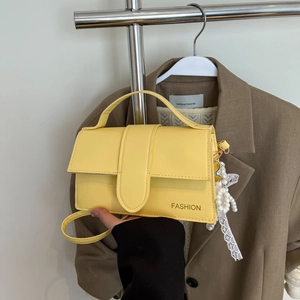 Close-up of bright yellow leather handbag with fashion text and pearl lace charm