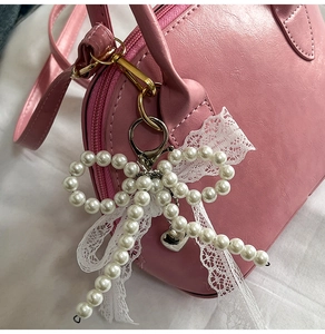 Detail of white pearl bow bag charm with lace ribbon and silver heart on pink leather bag