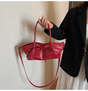 Détail d'un sac cabas en cuir rouge avec nœud décoratif et boucles dorées sur la bandoulière
