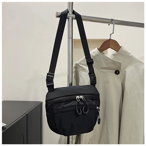 Close-up of black crossbody bag detail with dual zippers and adjustable woven strap