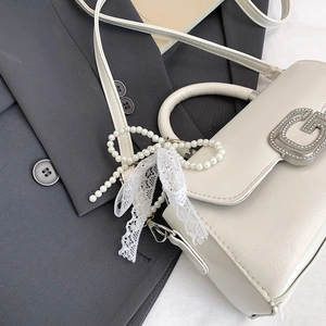 Detail of white mini bag with silver G-buckle and pearl lace bow on a grey blazer