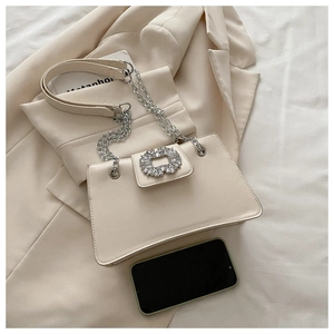 Detail of a creamy white crossbody bag with large round rhinestone buckle and chain strap