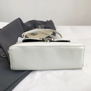Detailed close-up of a white textured handbag featuring a silver buckle and lace charm
