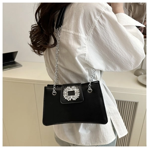 Detail of a black leather shoulder bag with a large crystal buckle and silver chain strap