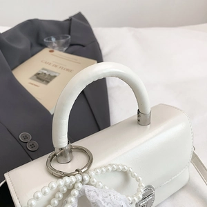 Detail of white leather handbag with pearl chain, lace accents and silver metal hardware