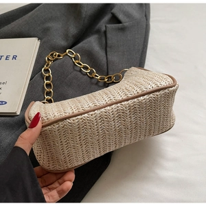 Close-up of woven straw shoulder bag featuring golden chain strap and brown piping detail