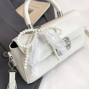 Detail of white handbag with pearl bow, lace decor, and metallic B-logo on leather texture