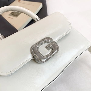 Close-up of white leather handbag with sparkling silver G-shaped rhinestone buckle detail