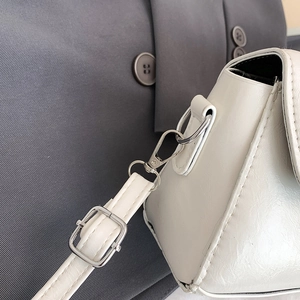 Close-up of white leather handbag featuring silver hardware and adjustable strap detail