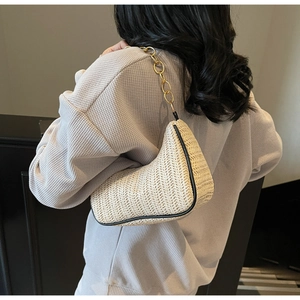 Detailed view of beige woven shoulder bag with black piping and gold metal chain strap