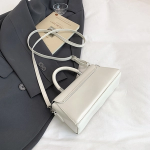 Detail view of cream rectangle handbag with silver hardware on a grey blazer