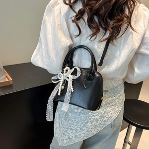 Elegant black shell bag with pearl lace bow charm shown on a model in a lifestyle setting