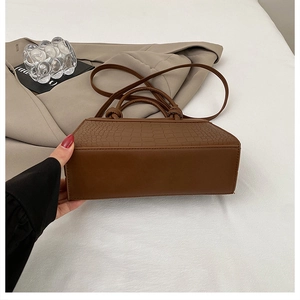 Detail of brown tote bag with crocodile texture and elegant knot handle design