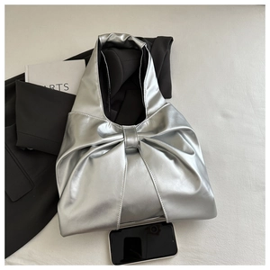 Detail of silver metallic tote bag with large bow design on a soft fabric background