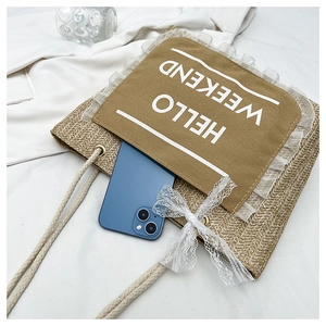 Detail of woven straw tote bag featuring Hello Weekend print and white lace bow decoration