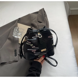 Detail of black canvas bucket bag with colorful wavy embroidery and drawstring closure