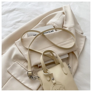 Detail of a beige mini tote bag with dog pendant and adjustable strap on a blazer