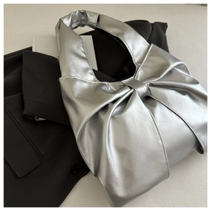 Close-up of a silver metallic bow-shaped tote bag on a black blazer with leather texture