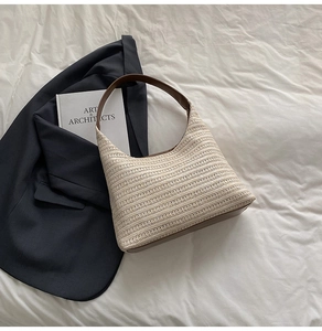 Detail view of woven straw tote bag with brown leather handles on a minimalist background