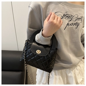 Detailed view of black quilted leather handbag featuring a golden turn-lock and chain strap