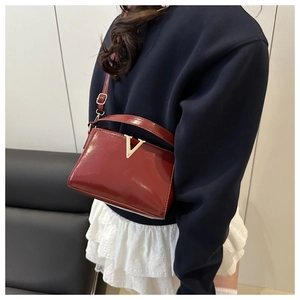Détail d'un sac bandoulière en cuir verni rouge avec une boucle en métal doré en forme de V