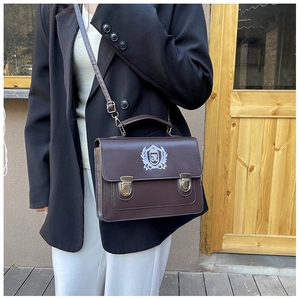Detail of vintage dark brown satchel with white crest embroidery and metal buckle closure