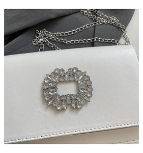 Detail shot of the luxury white leather handbag featuring a sparkling rhinestone buckle and silver chain