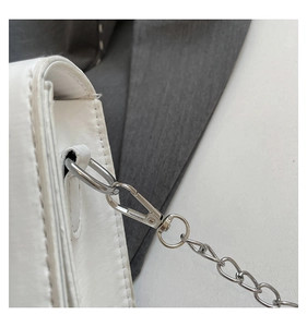Detail shot of silver metal chain hardware and d-ring on a white leather shoulder bag