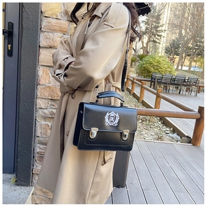 Detail of vintage academy style black shoulder bag with silver shield badge and metal buckles