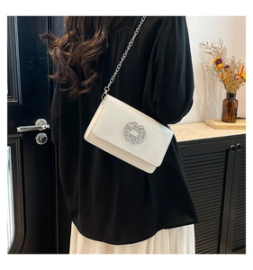 Detail view of white patent leather shoulder bag with sparkling crystal buckle on chain