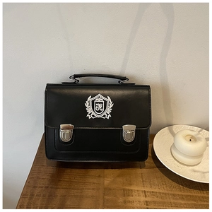 Detail of black vintage satchel showing white embroidered shield logo and silver buckles