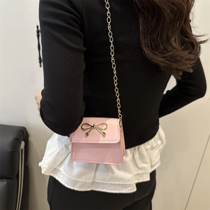 Chic mini pink crossbody bag with a gold bow accent and a delicate chain strap