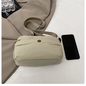 Detail view of khaki nylon crossbody bag with wide strap and metallic logo on textured fabric
