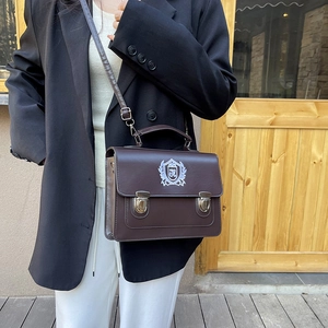 Retro brown satchel with shield embroidery shown as a stylish crossbody bag for women