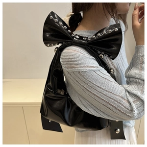 Detail of black patent leather underarm bag featuring oversized bow and silver studs