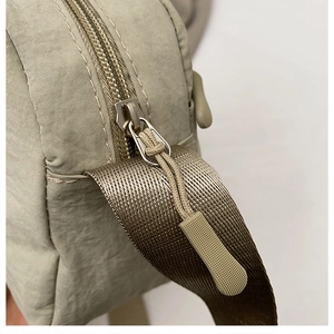 Detail shot of the metal zipper and woven strap on a khaki crossbody tote bag